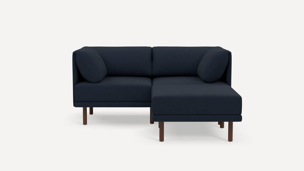 Modern navy blue sectional sofa with wooden legs, upholstered cushions, and round accent pillows, shown on a plain white background.