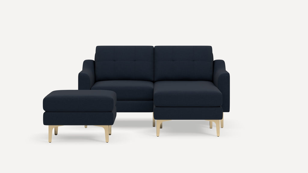 Dark navy blue sectional sofa with chaise and matching ottoman, featuring tufted cushions and light wooden legs.