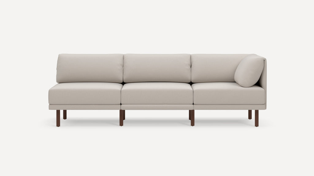 Modern beige modular sofa with three cushions, wooden legs, and a right-side armrest pillow, set against a plain background.