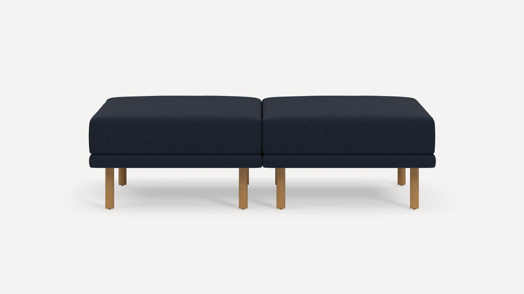 Modern navy blue upholstered double ottoman with natural wood legs, set against a plain light background.