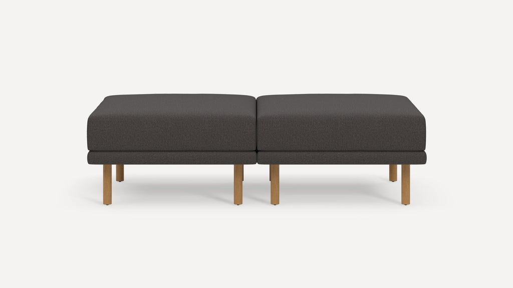 Two dark gray cushioned ottomans with wooden legs placed side by side on a white background.