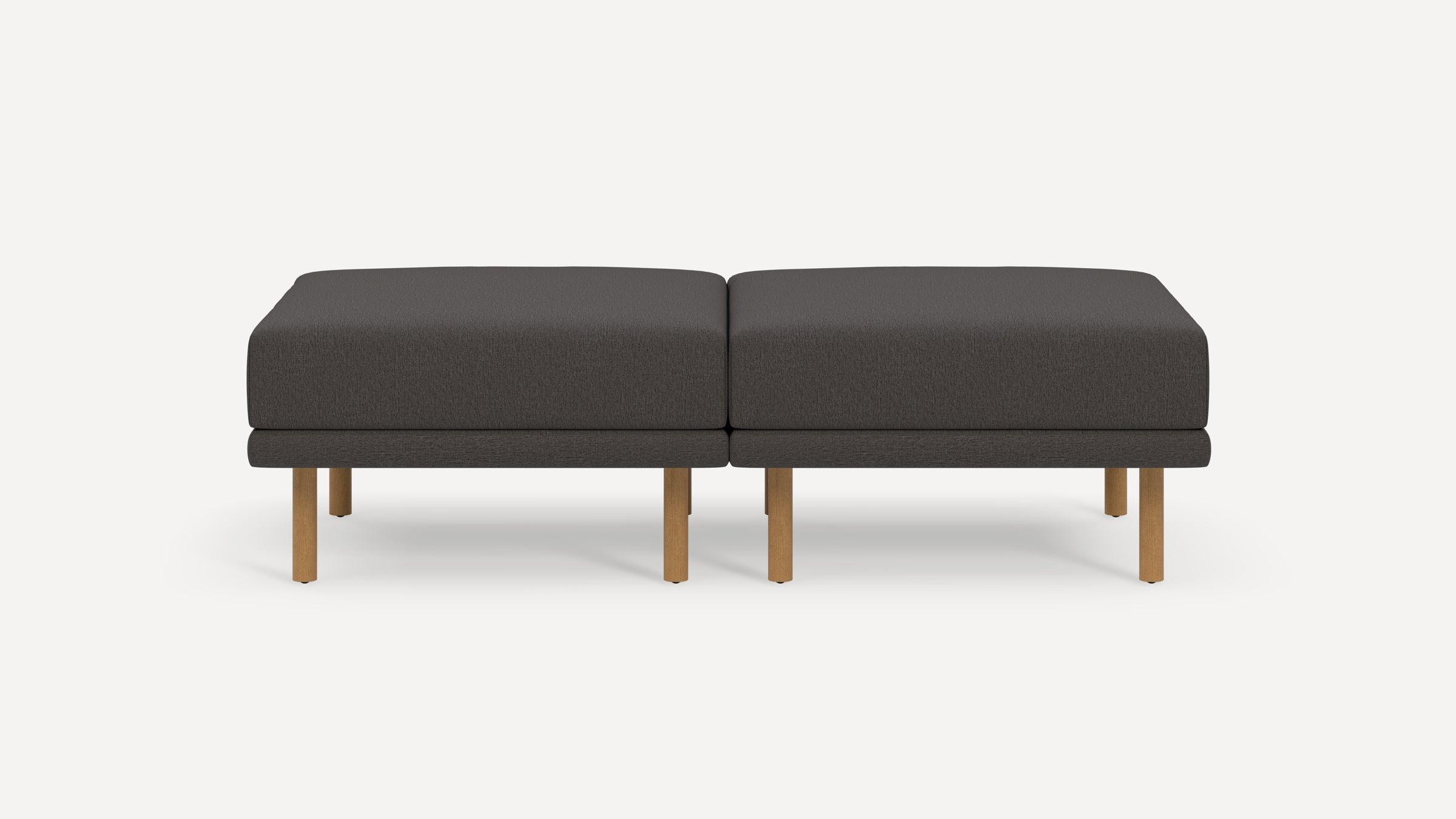Two dark gray cushioned ottomans with wooden legs placed side by side on a white background.