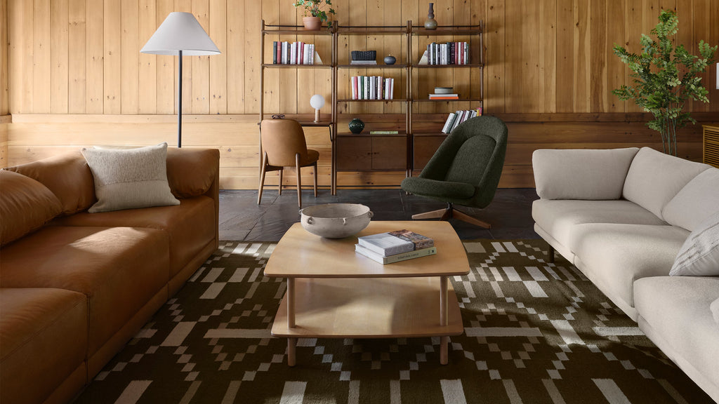 a living room with a brown leather couch, two brown chairs, a coffee table, and a bookcase on the wall