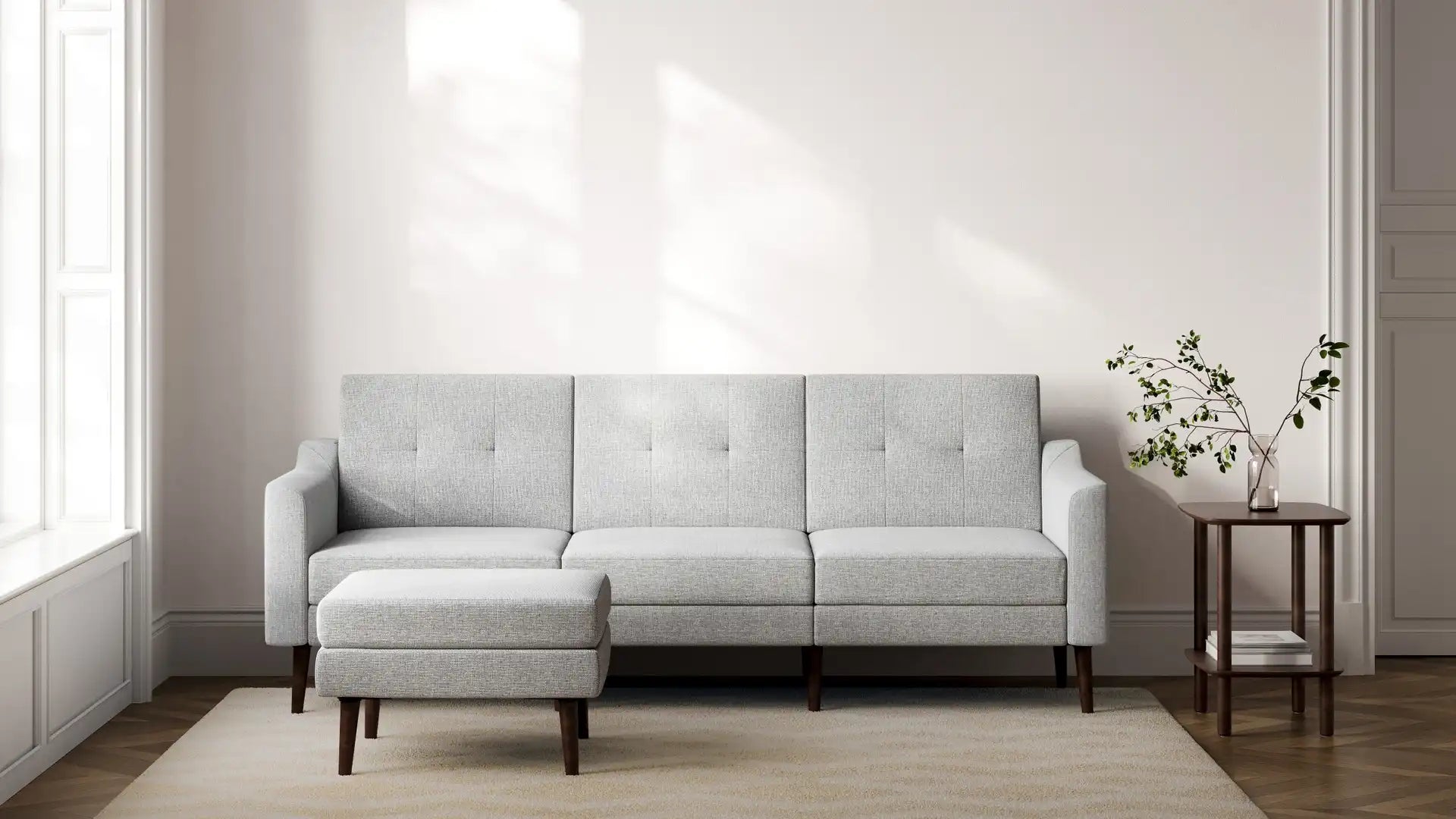 modern light gray fabric sofa with wooden legs and matching cushioned cushions on a beige rug in a white wall