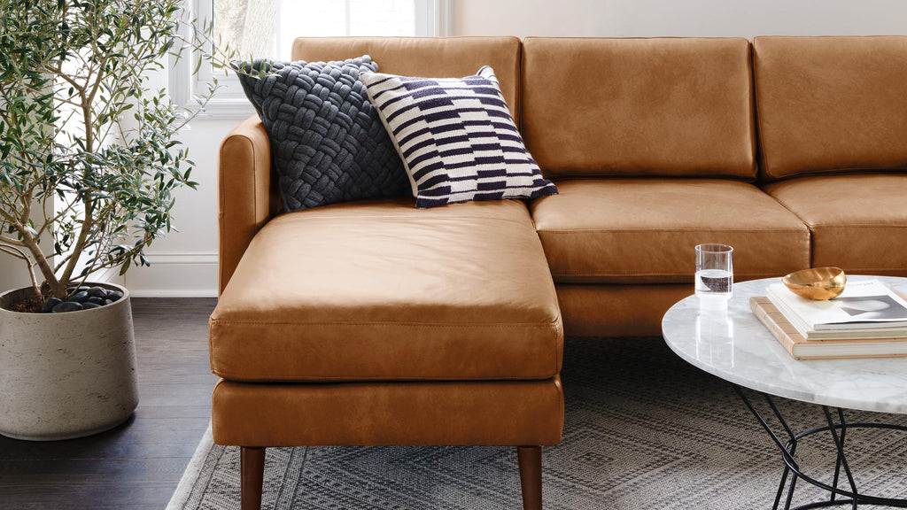 a modern living room with a brown leather sectional sofa, a white marble coffee table, and a black and white rug