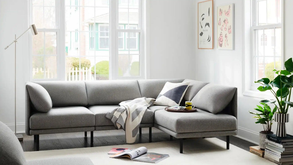 modern grey fabric sectional sofa with chaise lounge and matching cushions, featuring a plant, a book, and a magazine on the floor