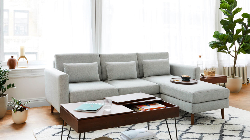 a modern living room with a gray sectional sofa, wooden coffee table, and a plant on the side of the couch