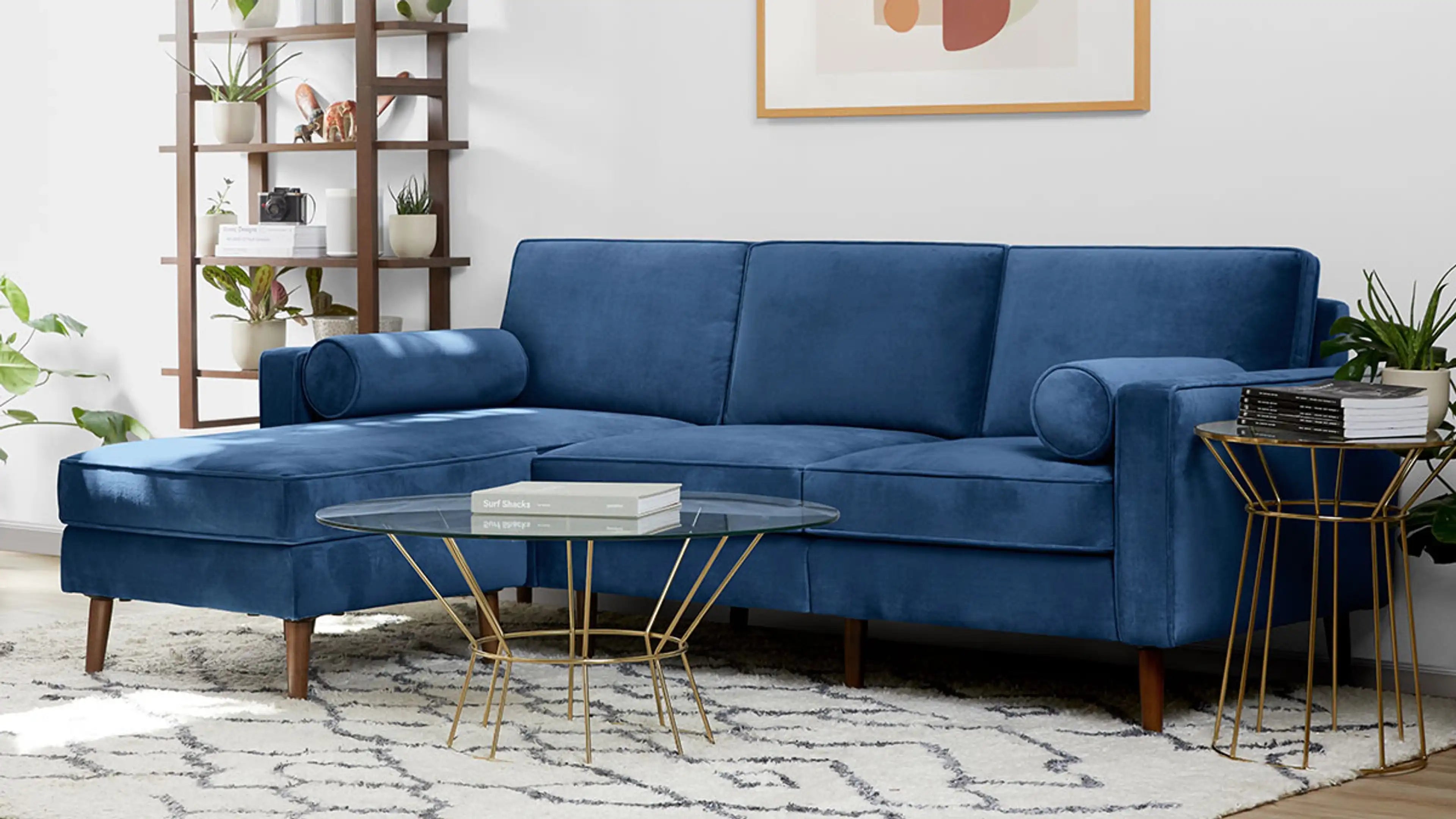 modern blue velvet sectional sofa with gold metal legs and matching cushioned sofa with matching ottoman, featuring a glass top table and plant