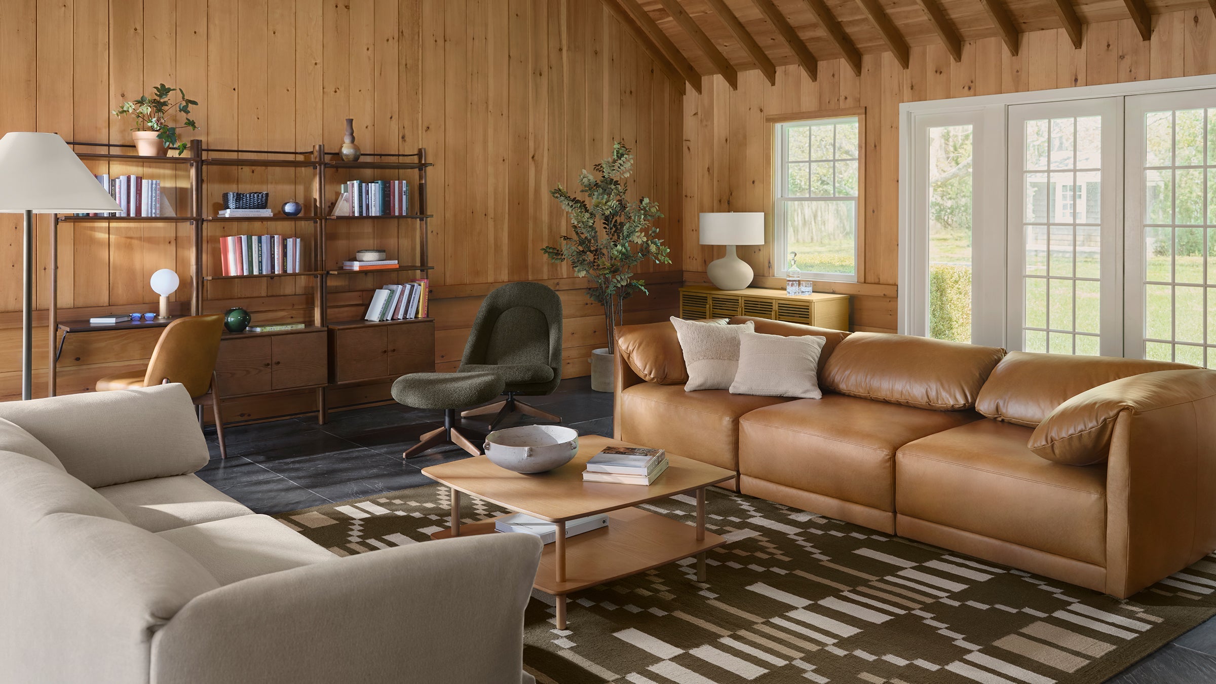 a living room with a brown leather couch, two chairs, a coffee table, and a bookcase