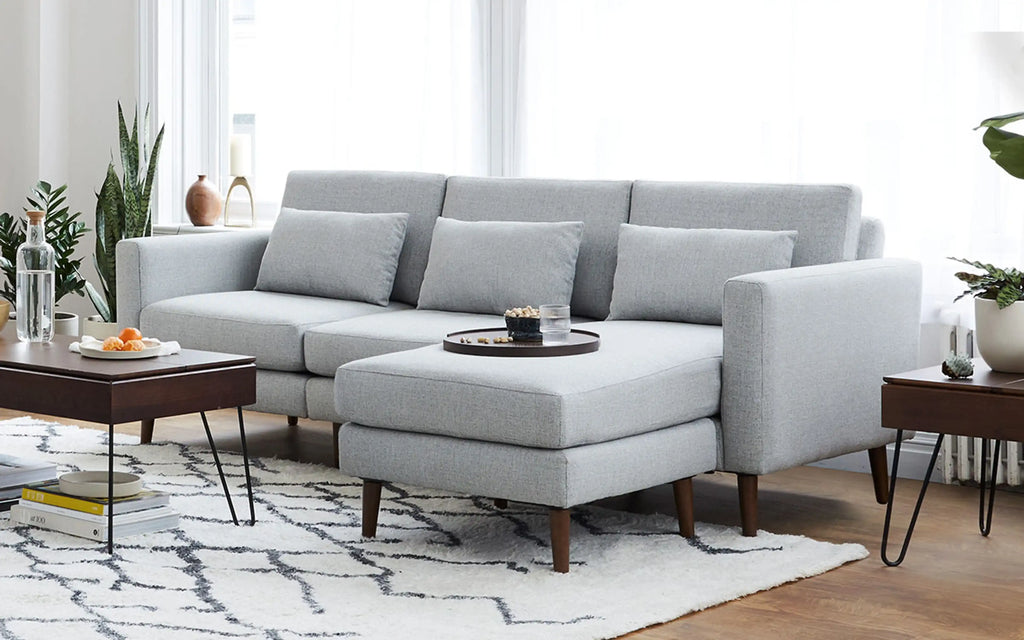 modern light gray sectional sofa with chaise lounge and matching ottoman on white rug in living room