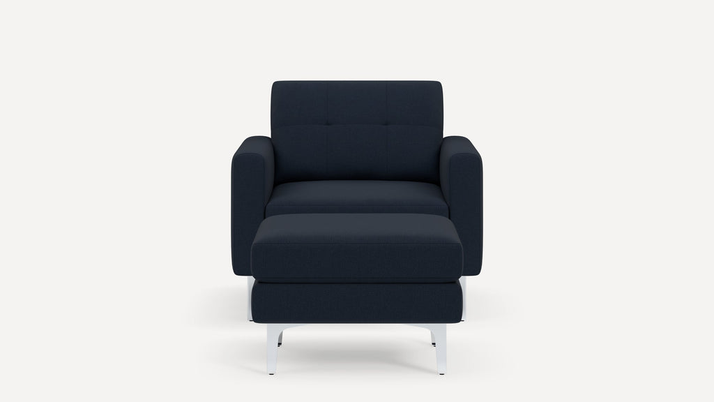 Front view of a modern dark blue upholstered armchair with a matching cushioned ottoman and white metal legs.