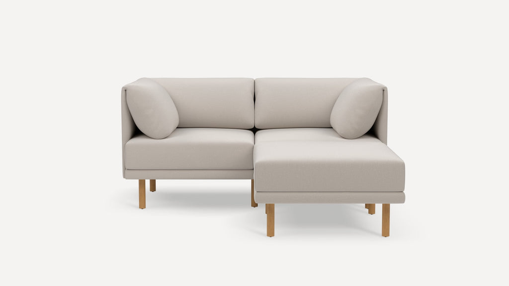 Light beige modern sectional sofa with wooden legs, two back cushions, and a right chaise lounge on a white background.