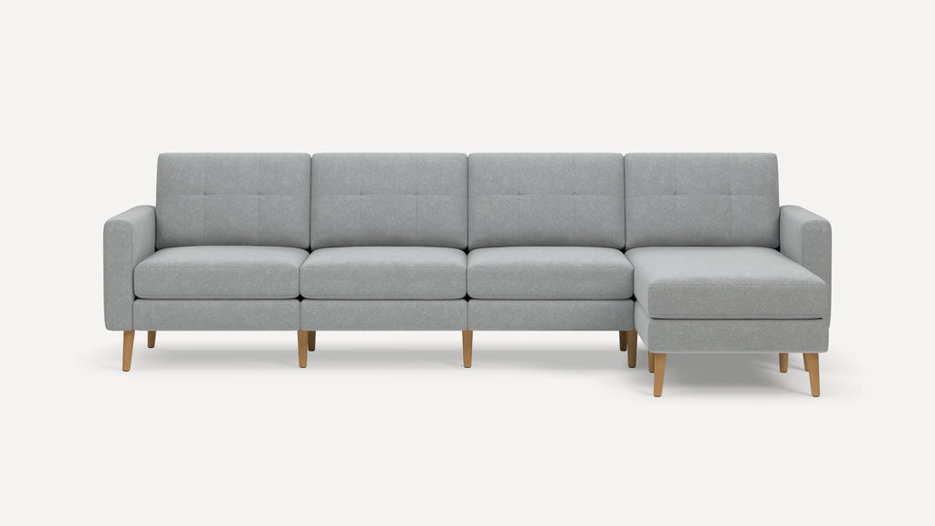 Modern light gray fabric sectional sofa with wooden legs, featuring a chaise lounge on the right side and tufted back cushions.
