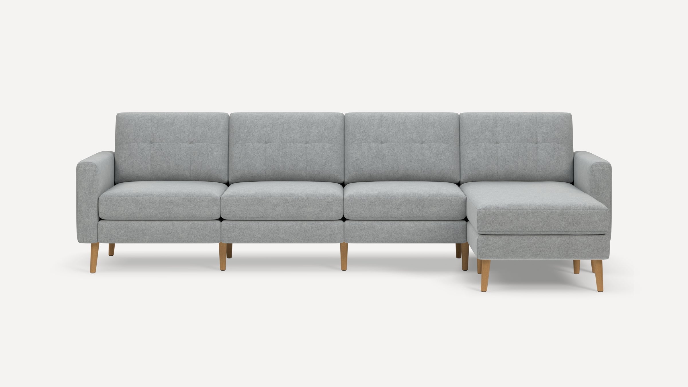 Modern light gray fabric sectional sofa with wooden legs, featuring a chaise lounge on the right side and tufted back cushions.