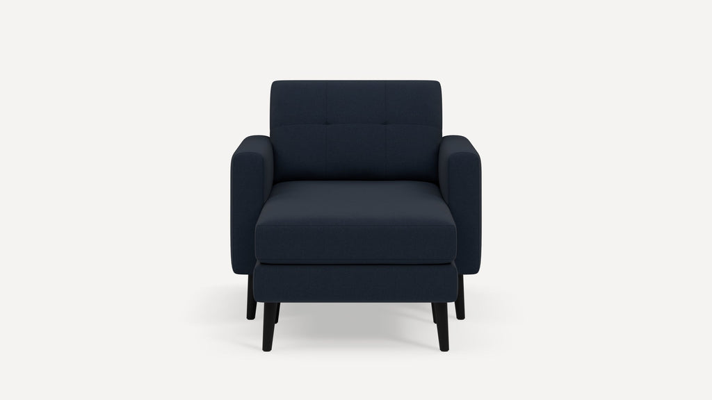 Front view of a modern navy blue upholstered armchair with matching ottoman and black wooden legs on white background.