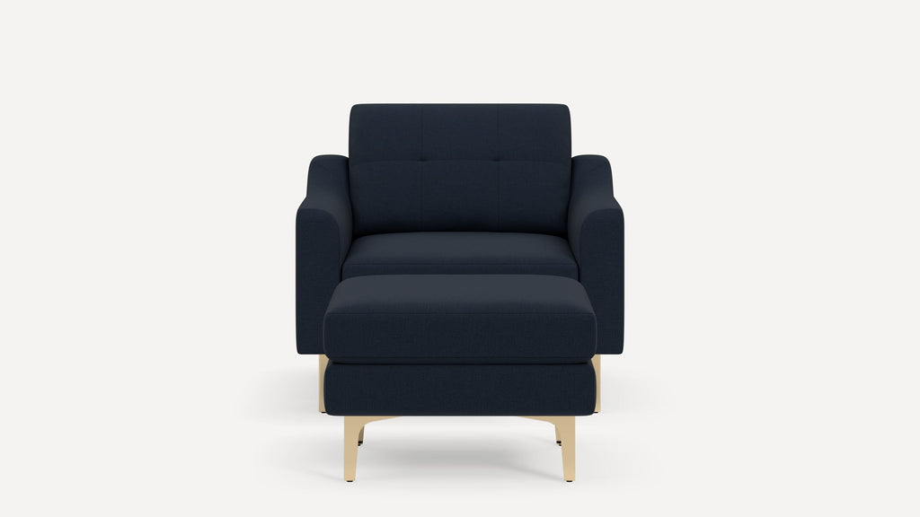 Modern navy blue armchair with matching ottoman, featuring cushioned seat, backrest with subtle tufting, and light wooden legs.