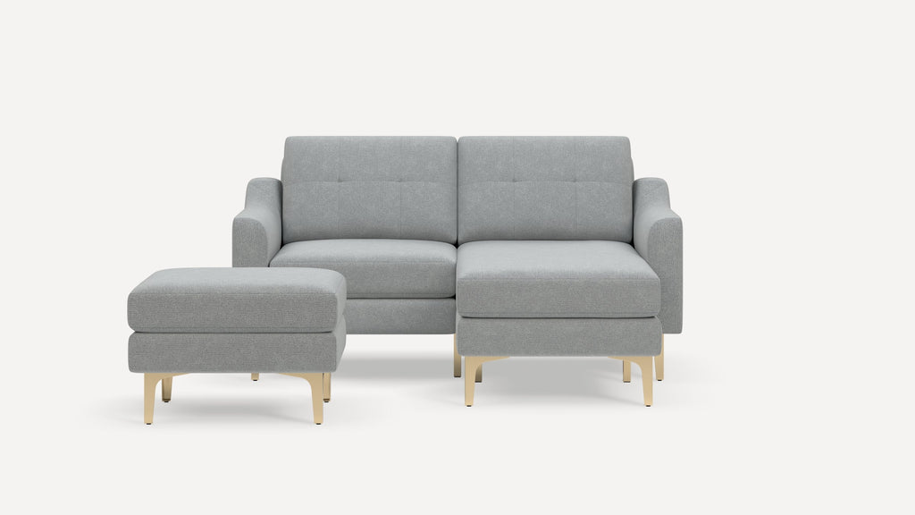 Modern light gray fabric sectional sofa with tufted back cushions and gold metal legs, accompanied by matching ottoman.