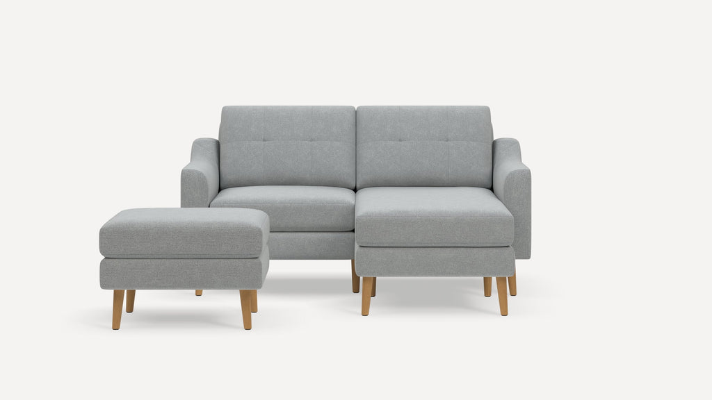 Light gray modern sectional sofa with tufted cushions and wooden legs, accompanied by a matching ottoman.