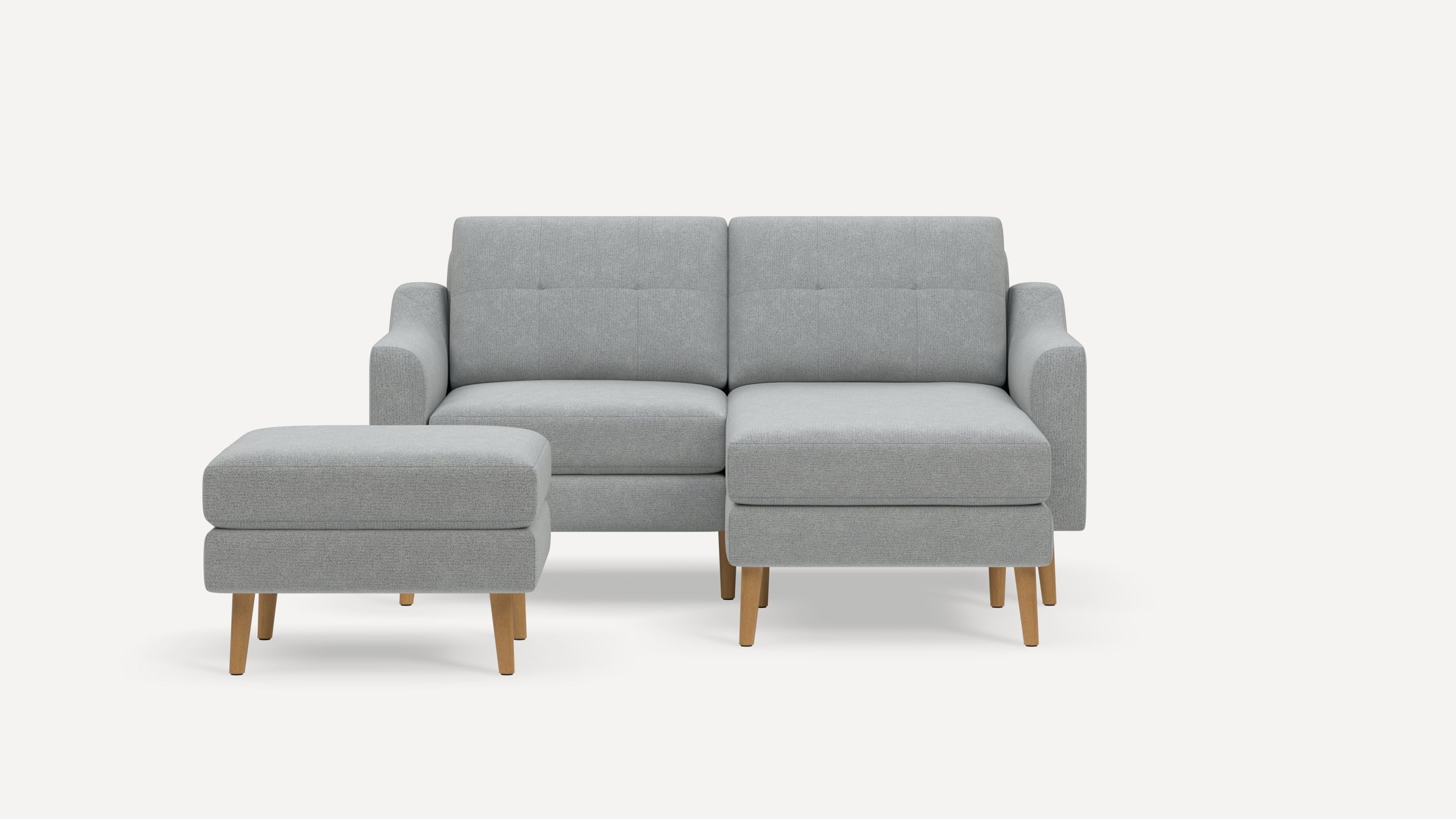 Light gray modern sectional sofa with tufted cushions and wooden legs, accompanied by a matching ottoman.