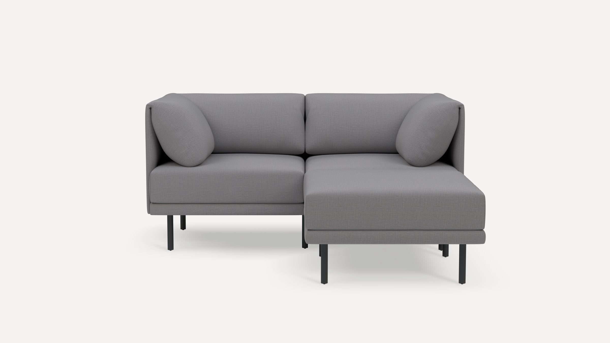 Modern grey fabric sectional sofa with metal legs and two matching cylindrical cushions, shown on a white background.