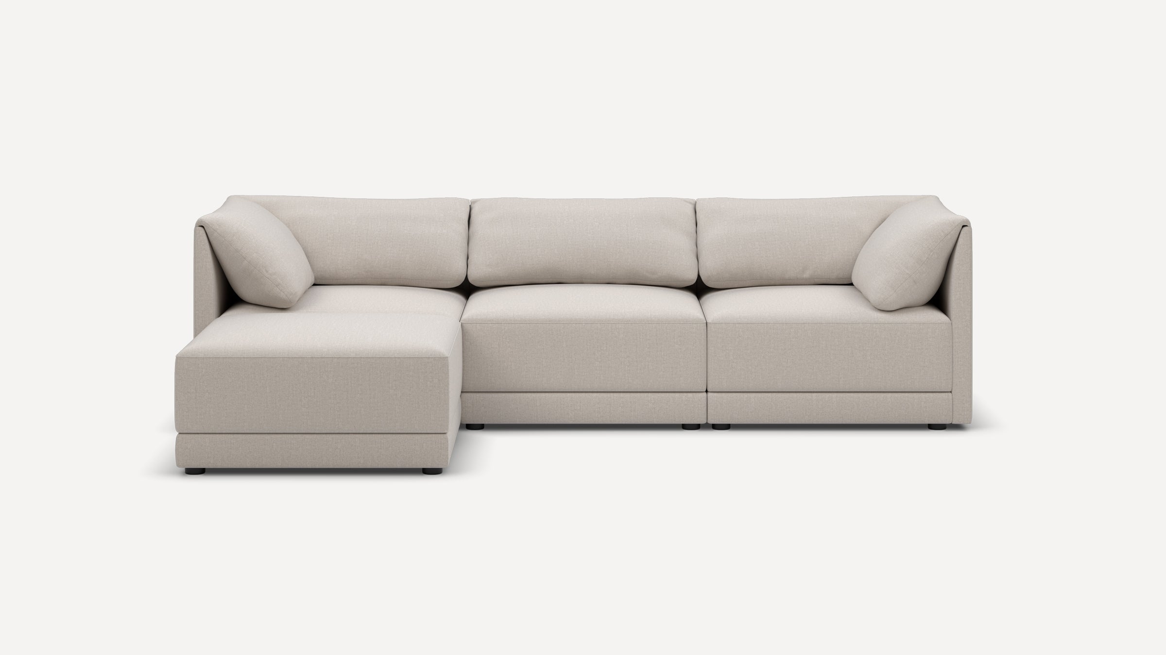 Modern L-shaped sectional sofa in light beige fabric with plush cushions and low black feet on a white background.