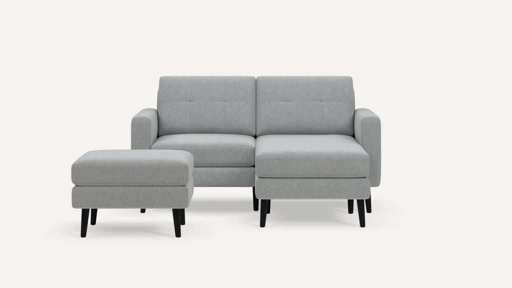 Light gray modern two-seater sofa with mid-century black wooden legs and matching ottoman on a white background.