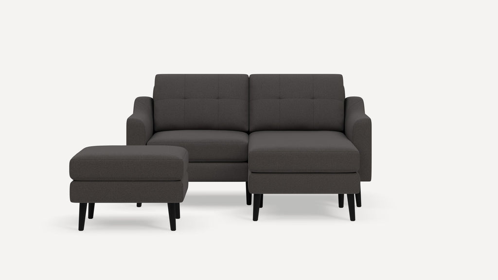Modern dark gray fabric sectional sofa with tufted back cushions and a separate matching ottoman on black legs.