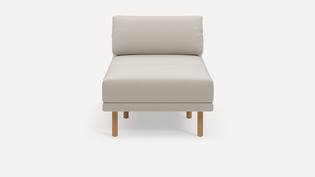 Front view of a modern beige chaise lounge with wooden legs and a cushioned backrest on a white background.