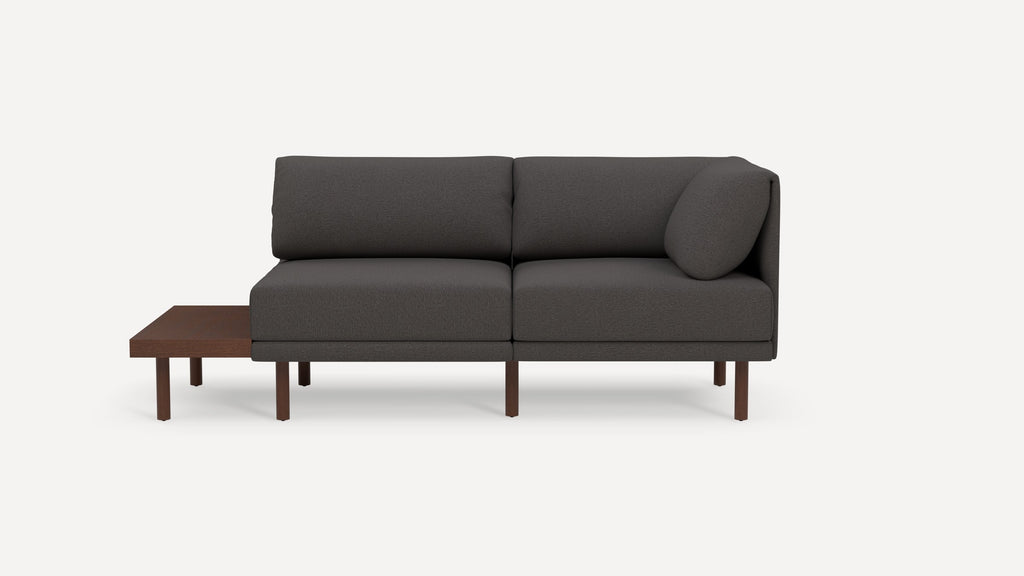 Modern dark gray fabric sectional sofa with wooden legs and an attached wooden side table on the left side.