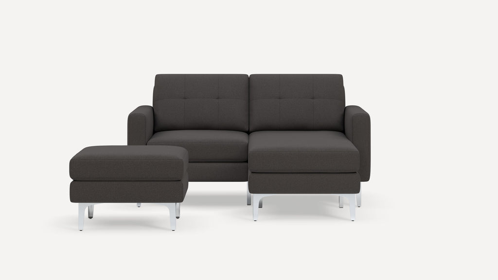 Modern dark gray fabric sectional sofa with tufted back cushions, armrests, and a matching ottoman on angled silver legs.