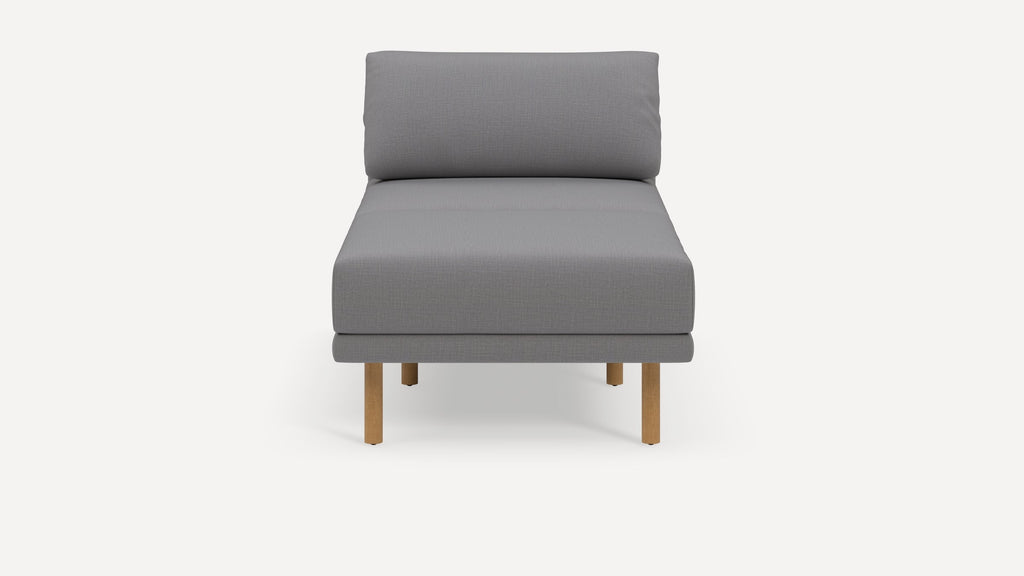 Modern armless grey upholstered chaise lounge with wooden legs, featuring a cushioned backrest and seat.
