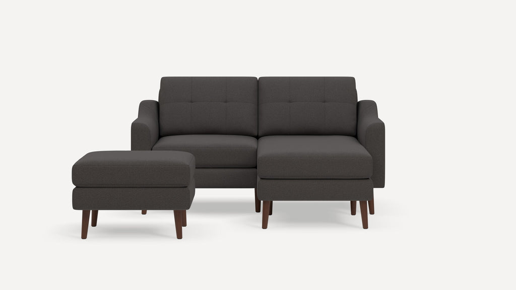 Dark gray fabric sectional sofa with tufted back cushions, wooden legs, and matching ottoman on a white background.