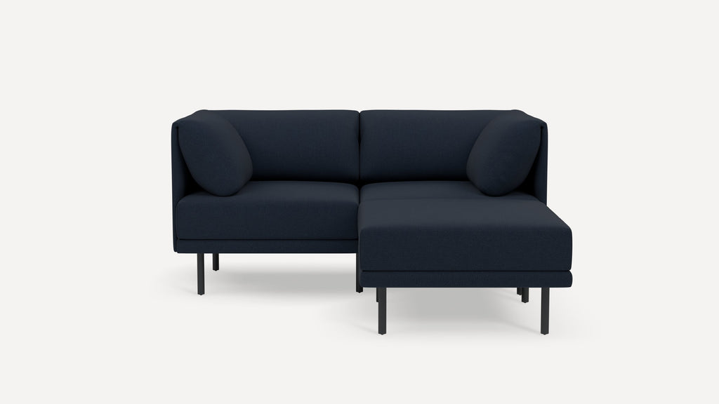 Corner sectional sofa with dark blue fabric upholstery, slim black metal legs, and rounded back cushions, shown on white background.