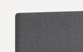 Close-up of dark gray upholstered fabric headboard with rounded top corner and textured weave pattern.