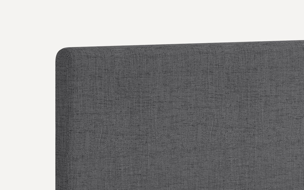 Close-up of dark gray upholstered fabric headboard with rounded top corner and textured weave pattern.