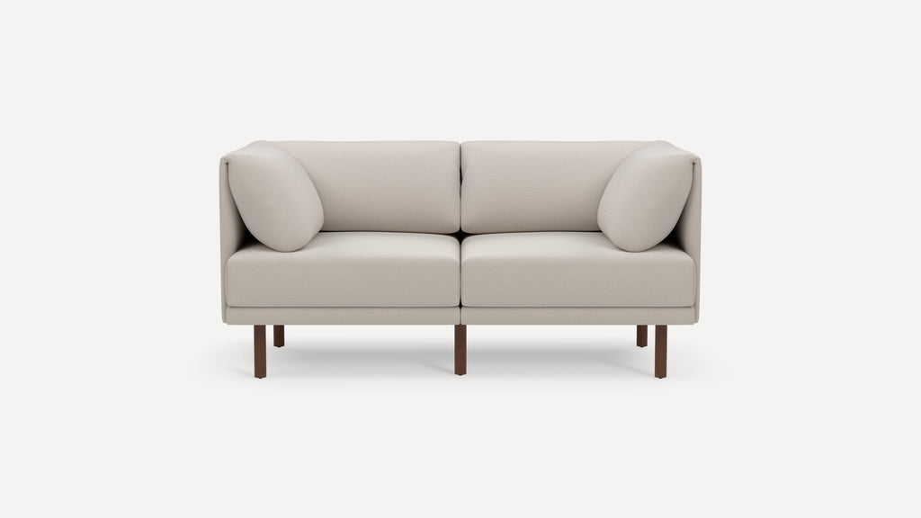Modern beige two-seater sofa with cushioned armrests and dark wooden legs on a plain white background.